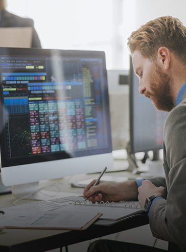 employee in front of monitor writing on paper
